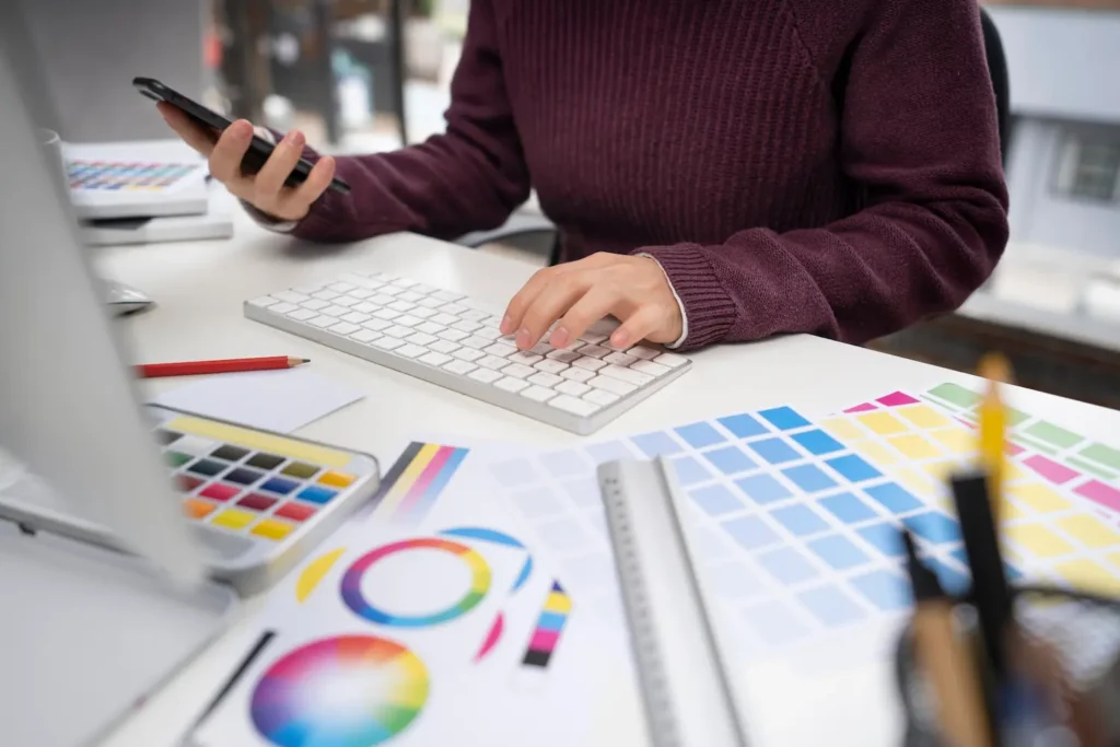 Persona sentada en un escritorio con un ordenador y varias paletas de colores explicándole a un cliente por correo qué es el diseño gráfico